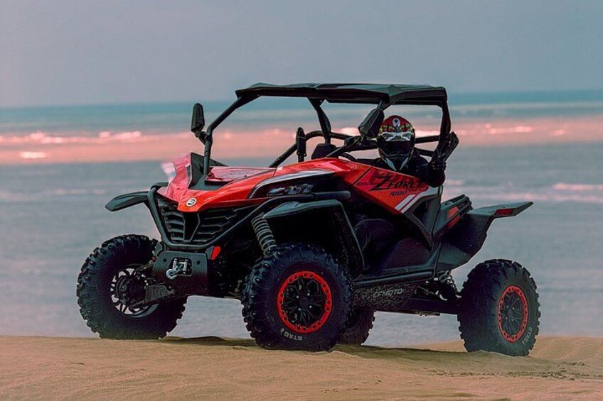 A red and black ATV with a person riding it on a beach with the ocean in the background. 2