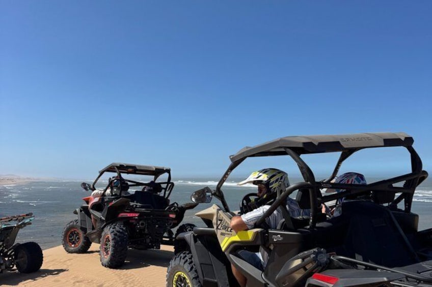 Deux véhicules tout-terrain sont stationnés sur une plage de sable, avec l’océan en arrière-plan. 2
