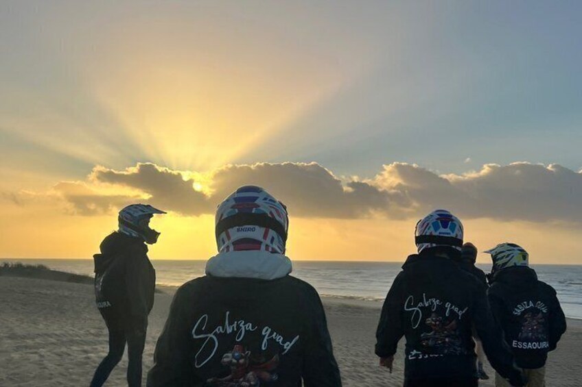 Quatre personnes se promènent sur une plage au coucher du soleil. 3