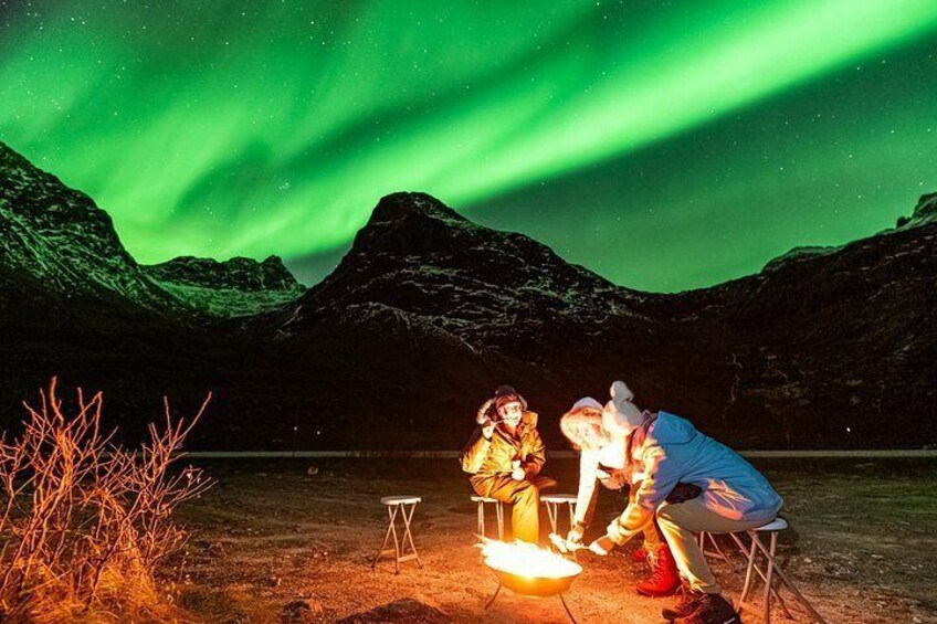 People around a campfire at night with the aurora borealis in the background. 1