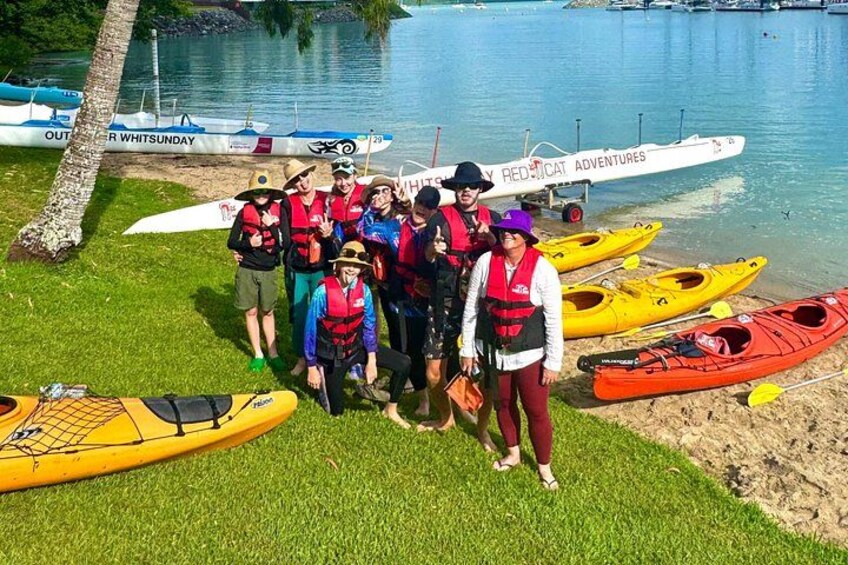 Un groupe de personnes portant des gilets de sauvetage se trouve au bord d’un lac, à proximité de kayaks et d’un bateau. 2