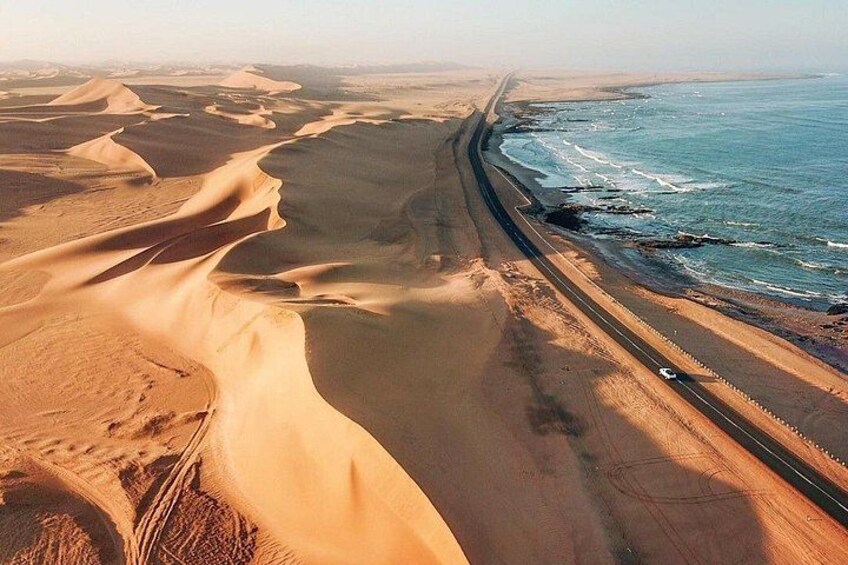 Eine Küstenlandschaft mit Dünen und einer Straße, die parallel zum Strand verläuft. 2