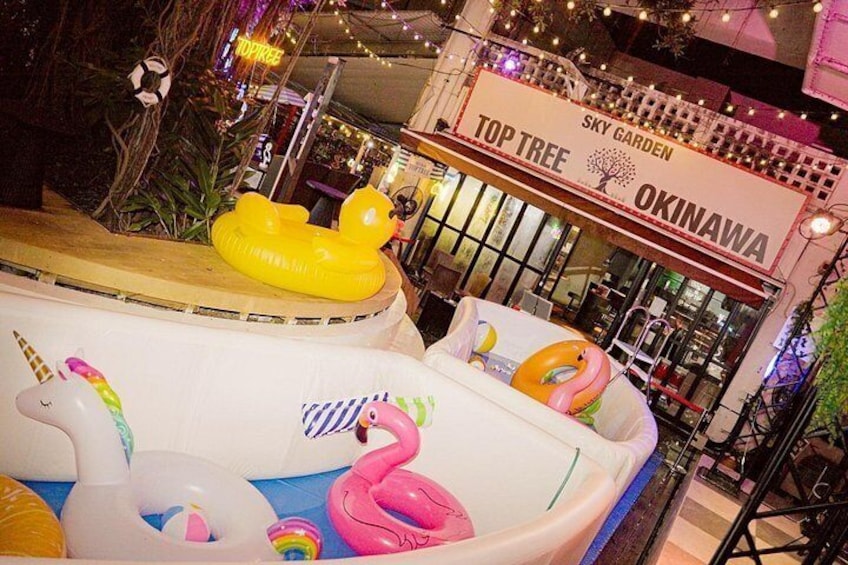 Inflatable pools with animal shapes, a sign for 'Sky Garden Top Tree Okinawa,' and a bar area in the background. 1