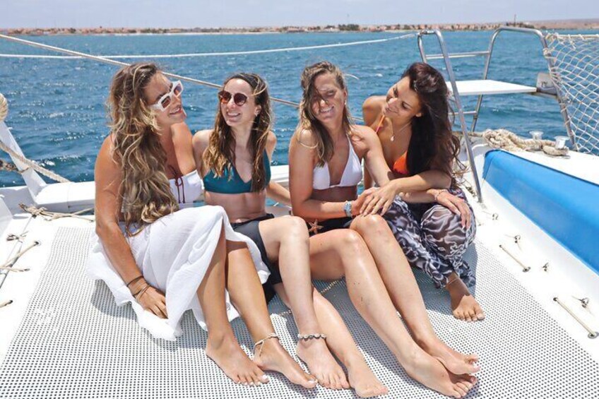 Quatre personnes sont assises sur le pont d’un bateau, devant une rambarde bleue et un filet blanc. 4