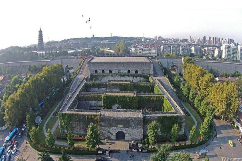 A historical fortification with a central tower, surrounded by greenery and modern buildings in the background. 4