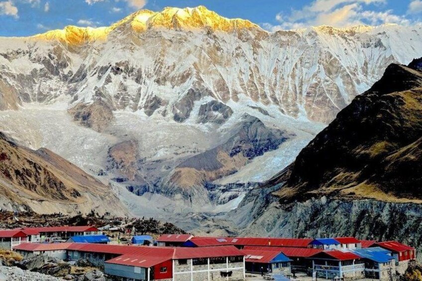 A mountainous landscape with a glacier, a small settlement with red-roofed buildings, and a clear sky. 4