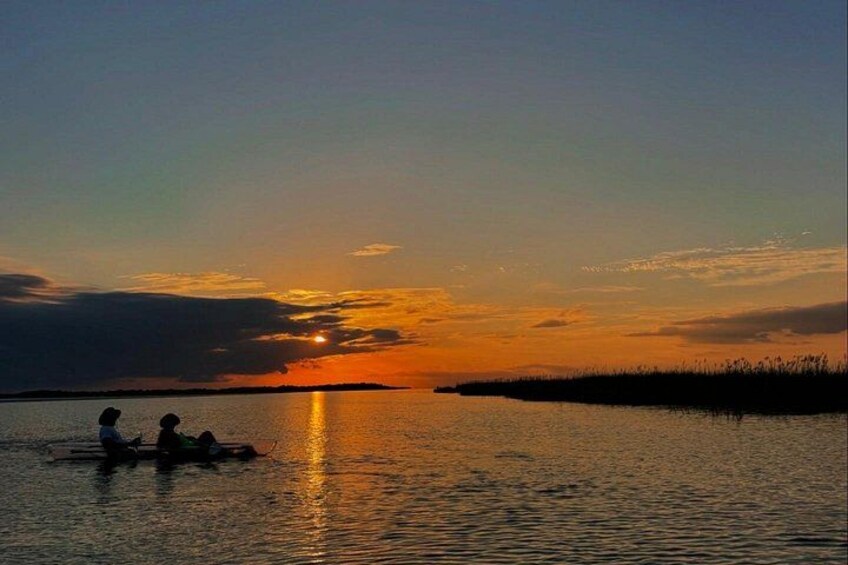 A sunset over a calm body of water with silhouettes of people on a boat. 4