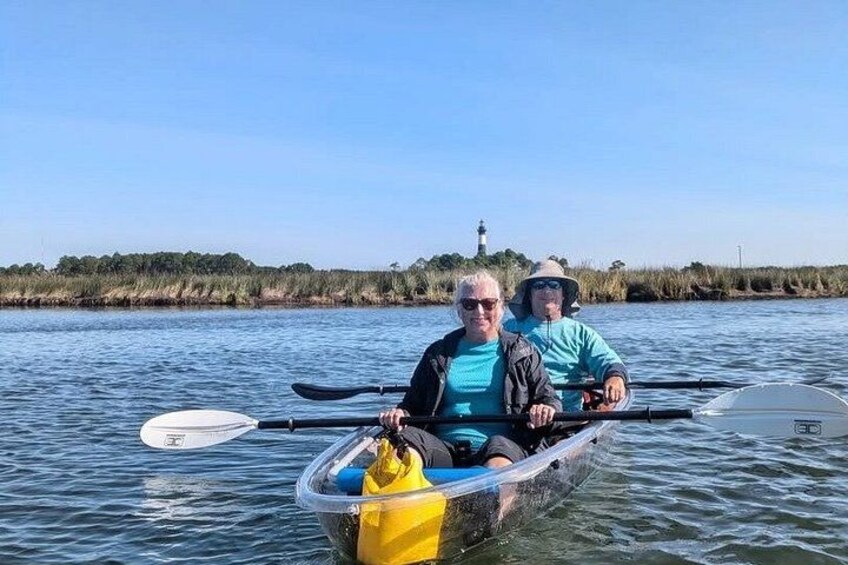 Two people in a kayak on a body of water with a lighthouse in the background. 2