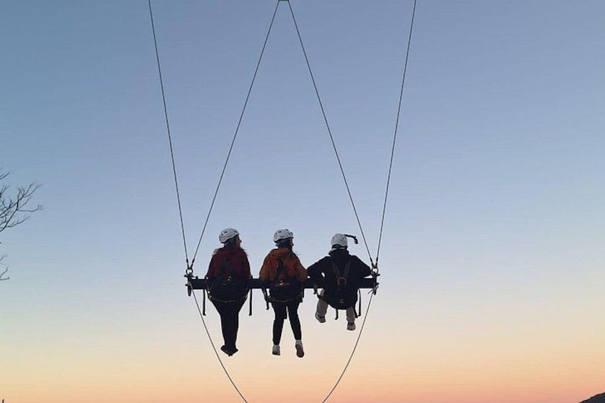 Three people suspended in the air by ropes against a clear sky. 3