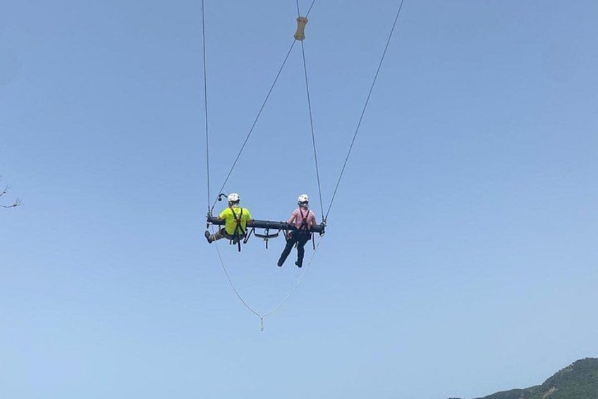 Two individuals suspended in the air, attached to a cable system, against a clear sky. 5