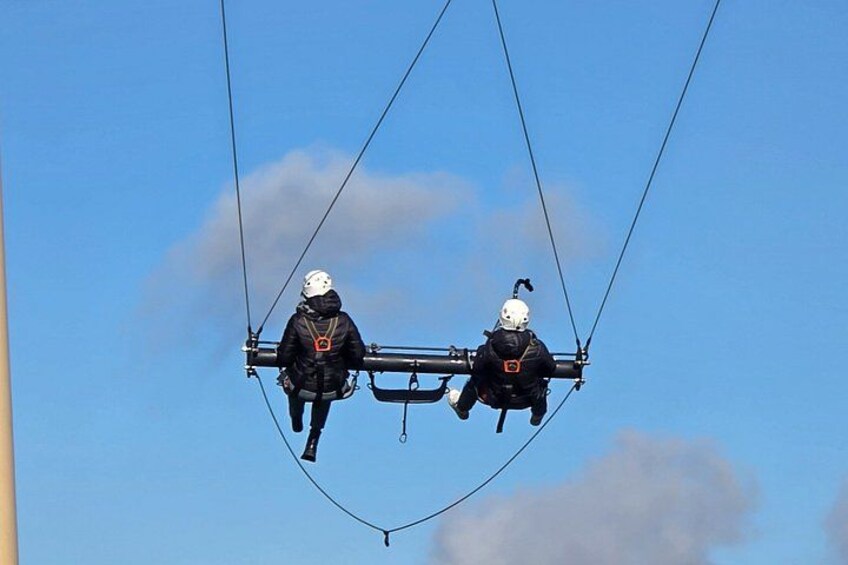 Two people suspended in the air by cables, wearing helmets and harnesses. 2