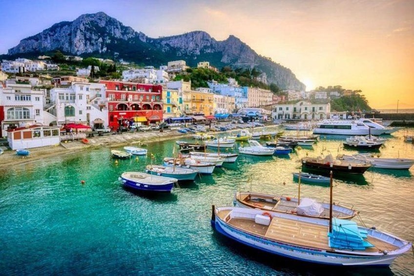 Una cittadina costiera con edifici colorati, imbarcazioni ormeggiate nel porto e una montagna sullo sfondo. 1
