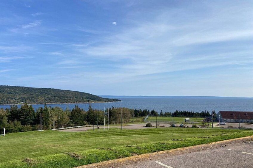 A grassy field with a road, a building, and a body of water in the distance. 3