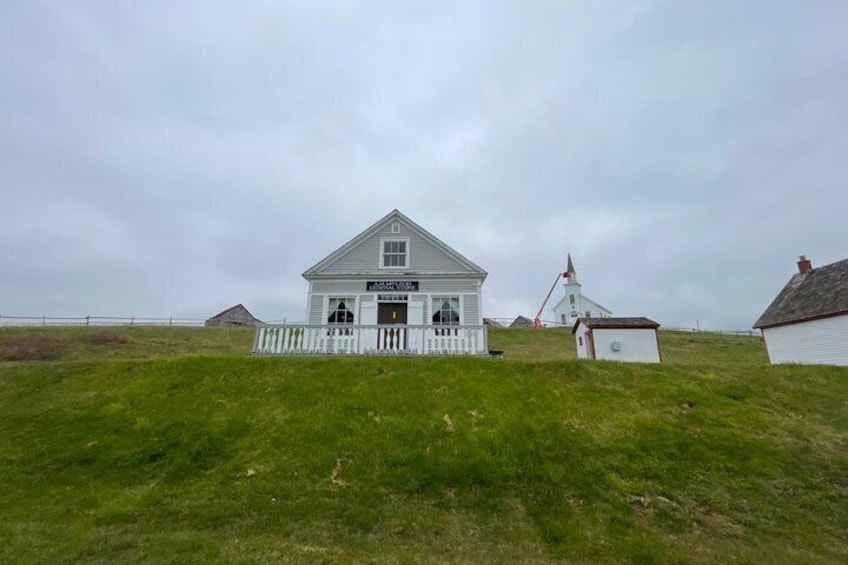 Eine weiße Kirche, ein weißer Zaun, ein kleines Gebäude und ein Leuchtturm auf einem grasbewachsenen Hügel. 5