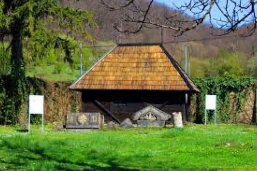 A wooden structure with a sloped roof, surrounded by greenery and trees. 3
