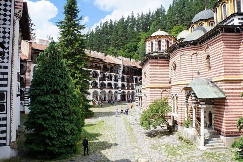 A courtyard with a large tree, a building with striped walls, and a person walking. 2