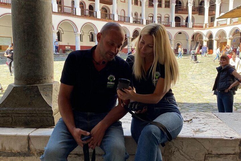 Two people sitting on a stone bench in a courtyard with columns and arches in the background. 3
