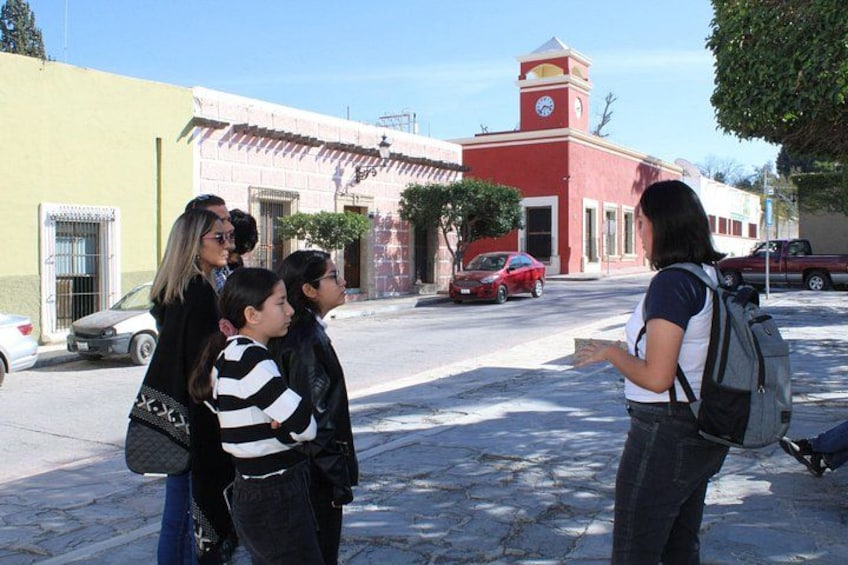 A group of people standing on a street, a red car parked on the side, and a building with a clock tower in the background. 3