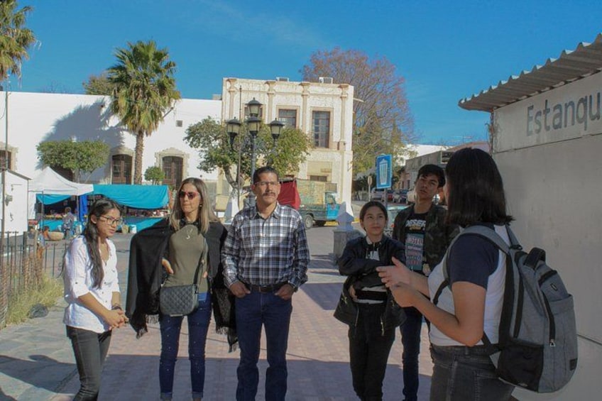 A group of people standing on a sidewalk in a historical area with buildings and a sign that reads 'Estanque.' 2