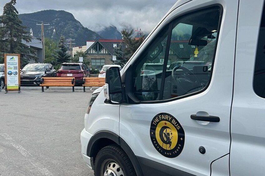 A white vehicle with a logo that reads 'The Fairy Bus' and a mountain in the background. 2