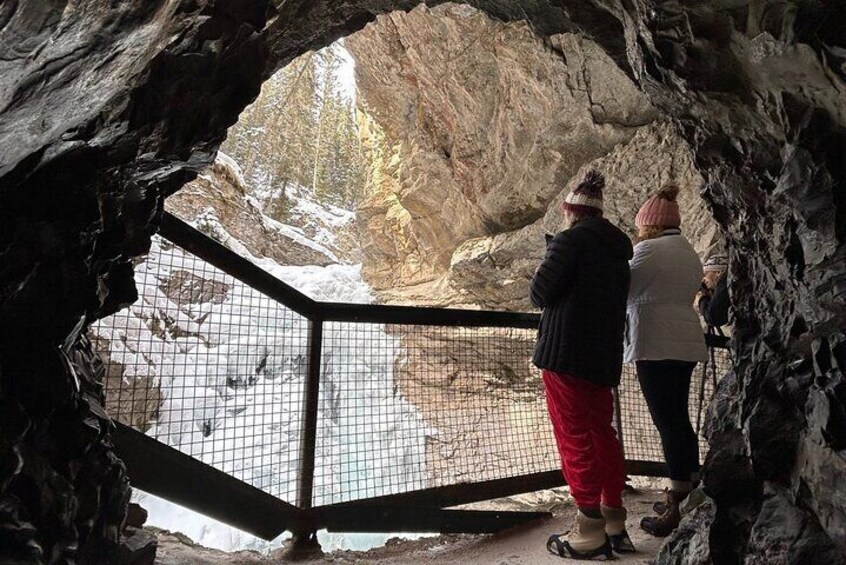 Two people observing a snowy landscape through a cave entrance. 5