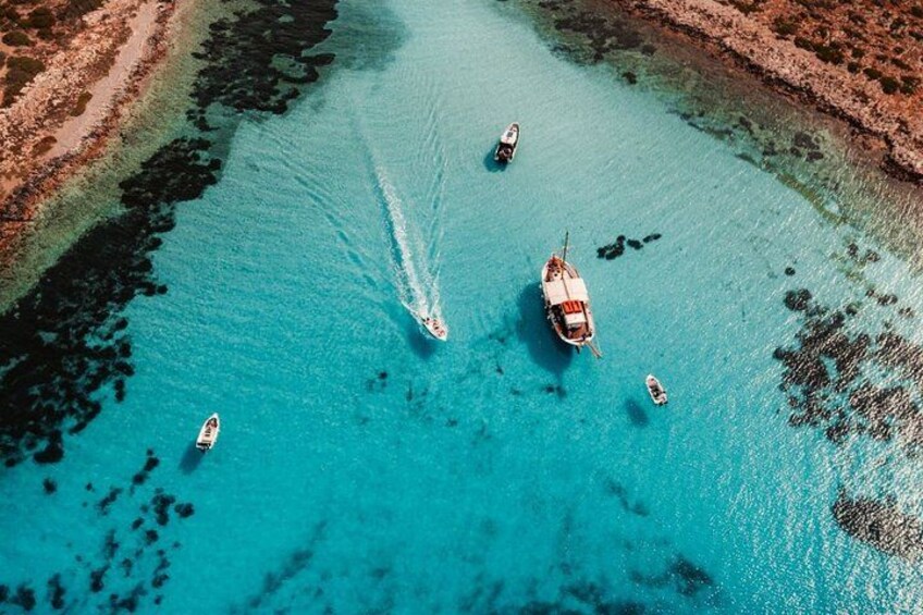Ein türkisfarbenes Meer mit Booten, einer felsigen Küste und strahlend blauem Himmel. 1