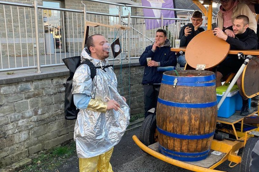 A person in a shiny costume standing next to a wooden barrel with a blue band. 5