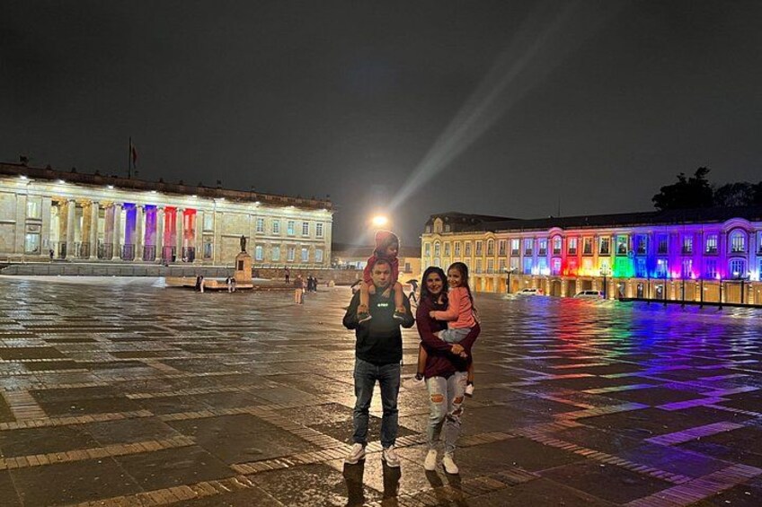 A plaza with illuminated buildings and a statue in the center. 2