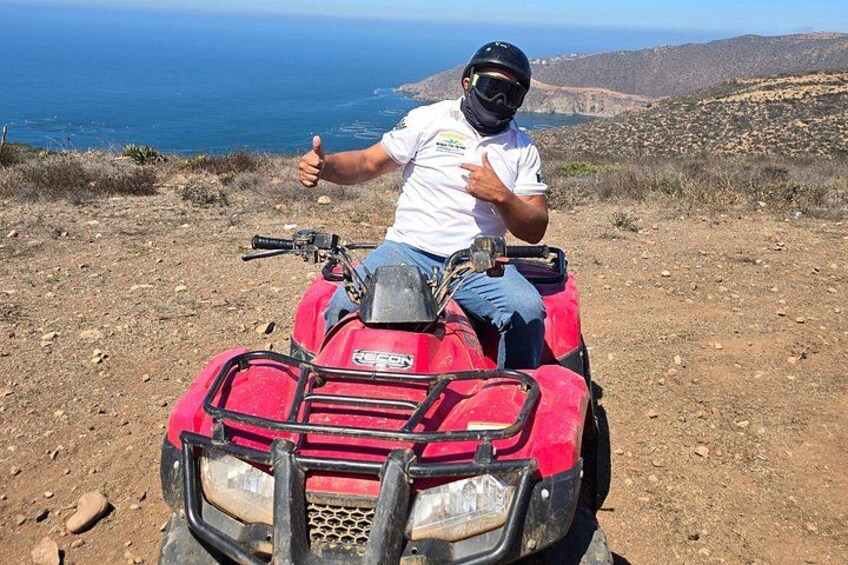 Une personne est assise sur un quad rouge, sur un terrain accidenté, avec une étendue d'eau en arrière-plan. 1