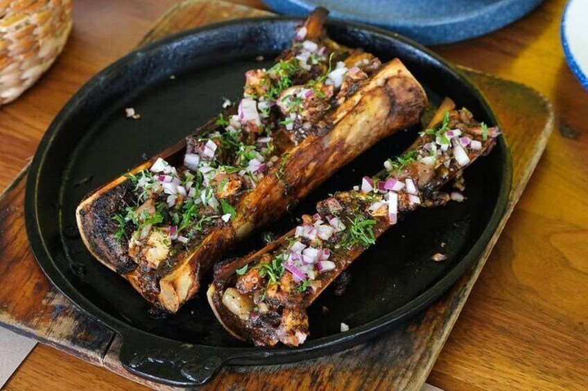 Dos costillas de cerdo a la parrilla adornadas con cebolla picada y hierbas sobre un plato negro. 2