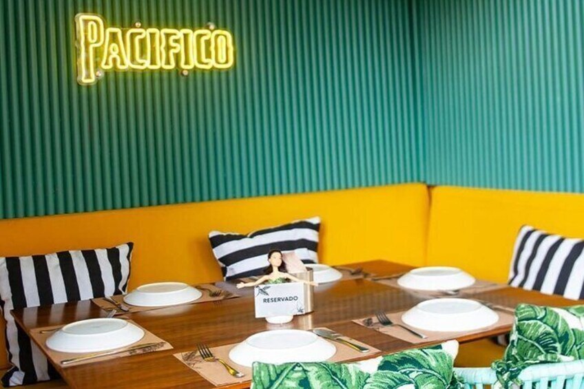 Interior de un restaurante con un letrero de neón que dice 'PACIFICO', una mesa de madera dispuesta con platos, cubiertos y un cartel de 'RESERVADO'. 4
