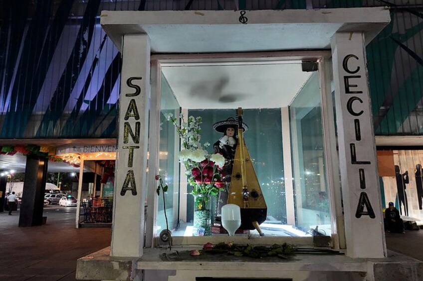 A glass display case with a statue of a woman in a sombrero and a guitar, labeled 'SANTA' and 'CECILIA.' 4