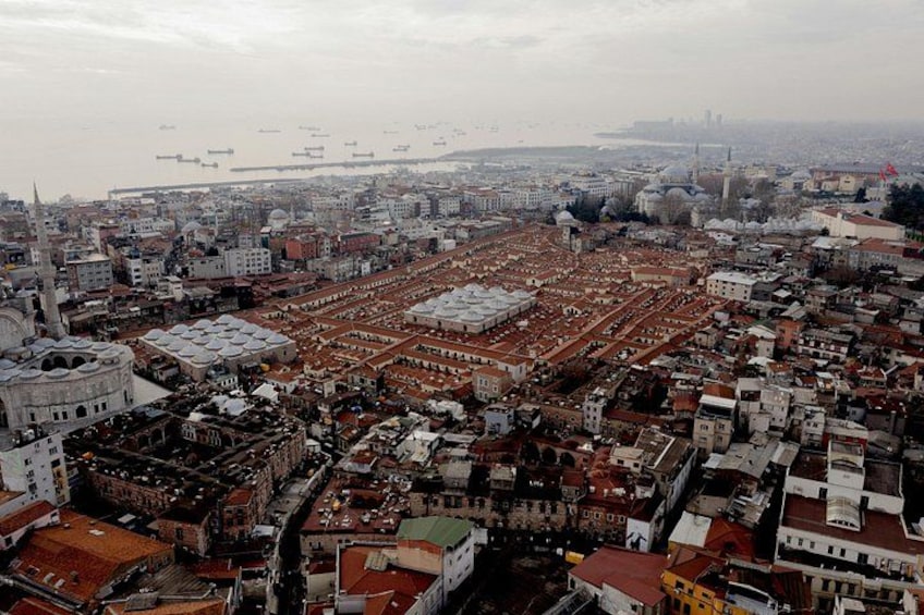 Una zona urbana densamente popolata, con numerosi edifici, una moschea importante con una cupola e un'ampia distesa d'acqua sullo sfondo. 1