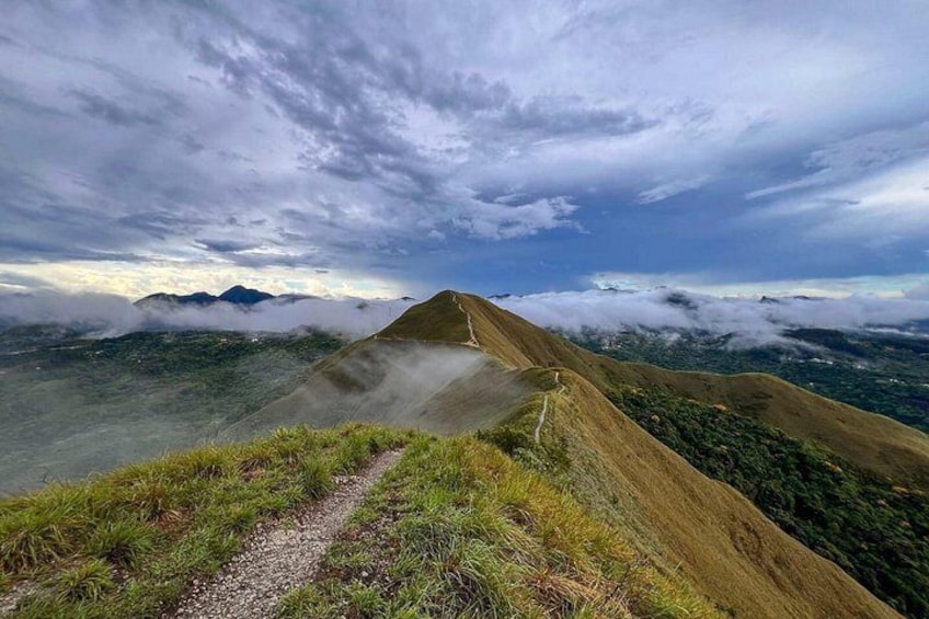 Paisaje montañoso con un sendero serpenteante, vegetación exuberante y cielo nublado. 4