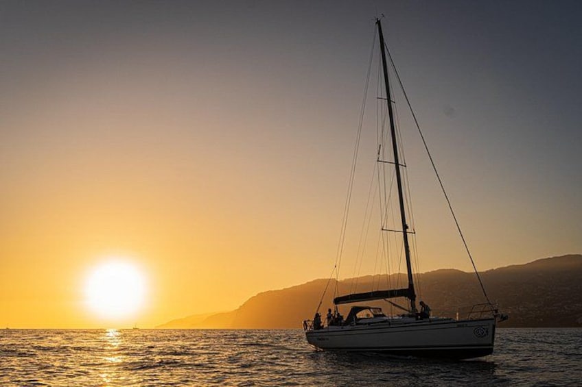 Een zeilboot op kalm water tijdens zonsondergang, met een heldere lucht en verre bergen. 3