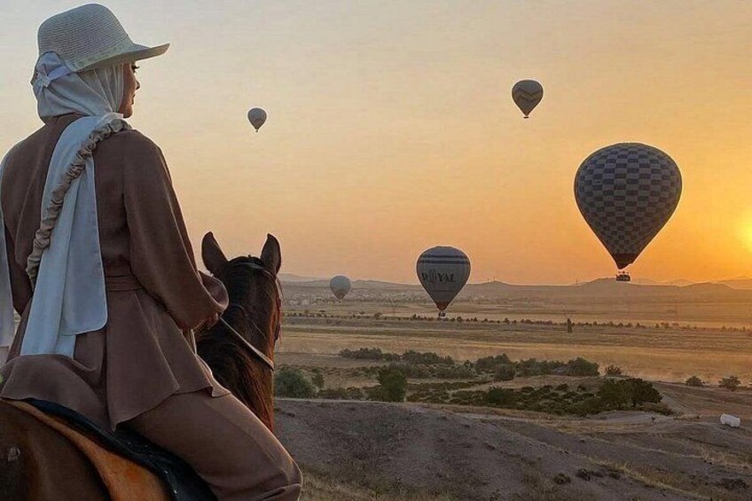 Una persona montando a caballo, globos aerostáticos al fondo y un atardecer. 4