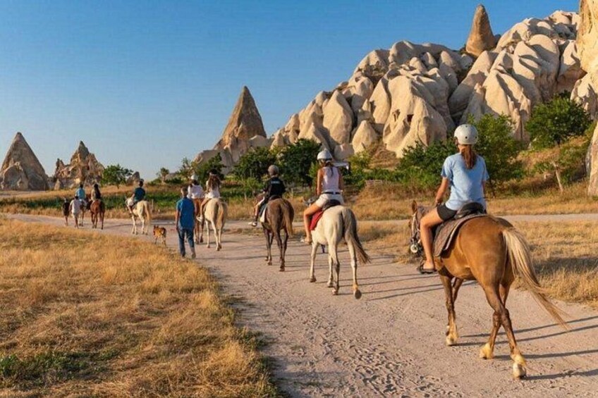 Un grupo de personas montando a caballo por un sendero de tierra con formaciones rocosas características al fondo. 1