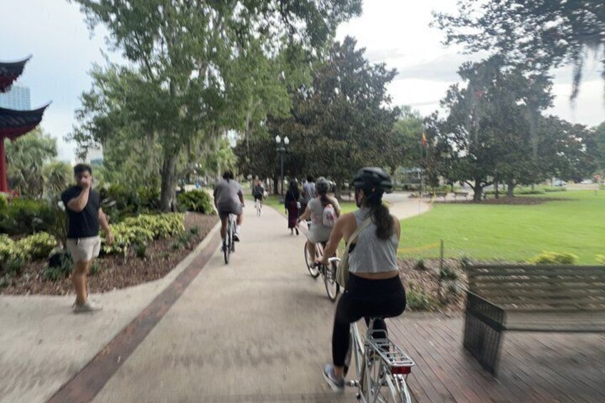 A group of cyclists on a paved path in a park with trees and a traditional building. 5