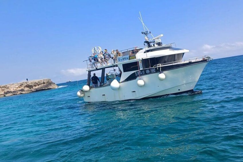 A white boat with people on board, sailing on clear blue water near a rocky shore. 4