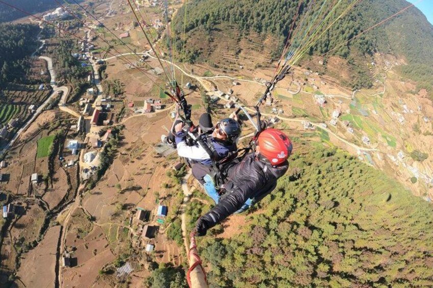 A person paragliding over a mountainous area with visible houses and terraced fields below. 4