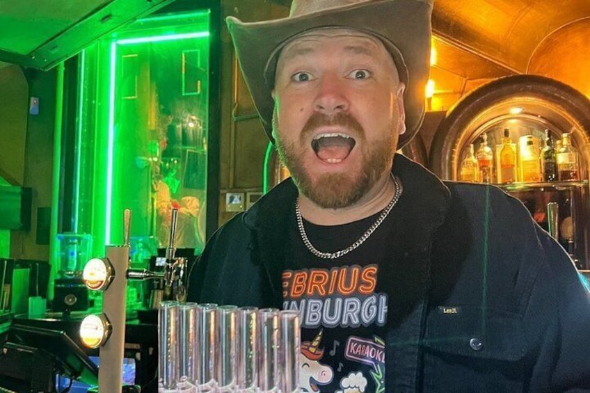 A person wearing a hat and a t-shirt with 'BRIOUS' and 'STUBBURG' text, standing in a bar with a beer tap and bottles in the background. 3