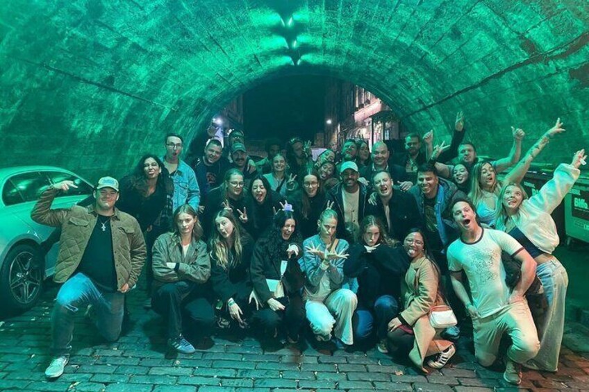 A group of people posing in a tunnel with a car parked outside. 5