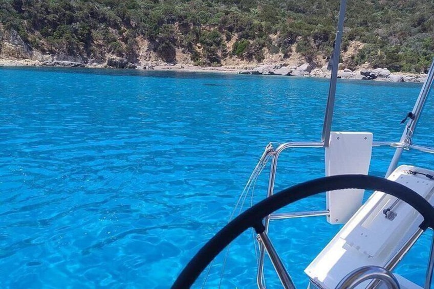 A boat on clear blue water with a rocky coastline in the background. 2