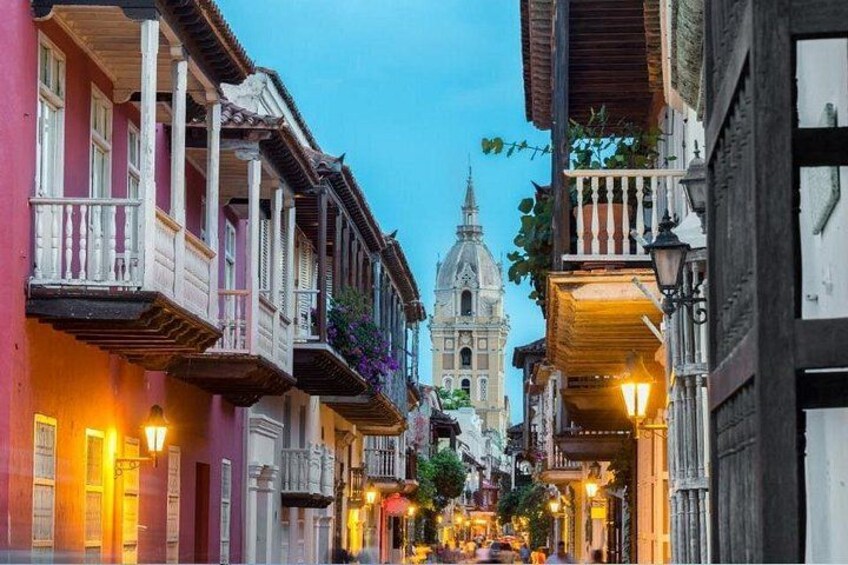 A street with colorful buildings, a church, and street lamps. 1