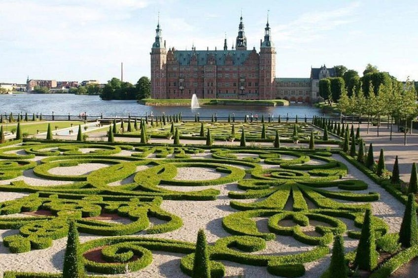 A formal garden with geometric patterns, a river, and a historic building in the background. 3