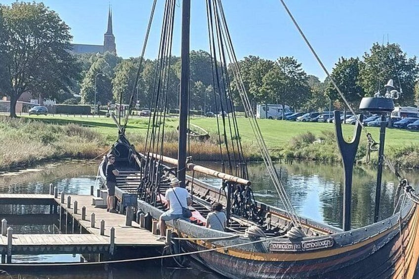 A traditional sailing boat docked at a pier with a church and parking lot in the background. 2