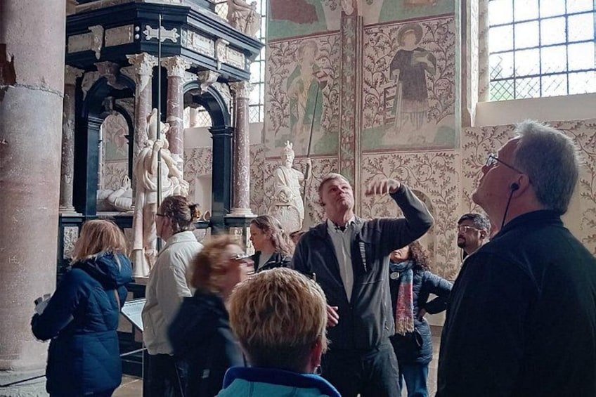 A group of people inside a building with classical architecture, including columns and detailed wall paintings. 5