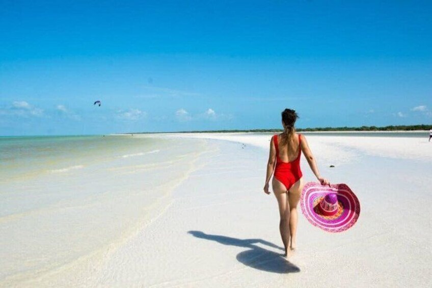 A person in a red swimsuit walking on a sandy beach with clear skies. 2