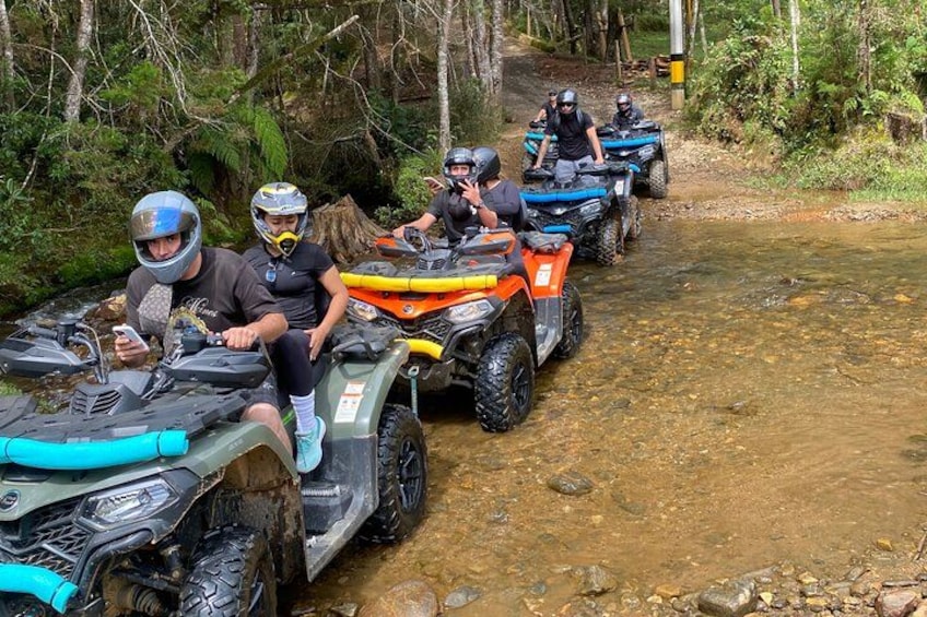 People riding ATVs on a muddy trail surrounded by trees. 5