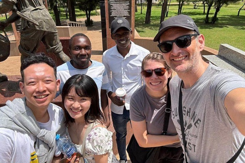 A group of people posing for a photo in a park with a statue and a monument in the background. 4